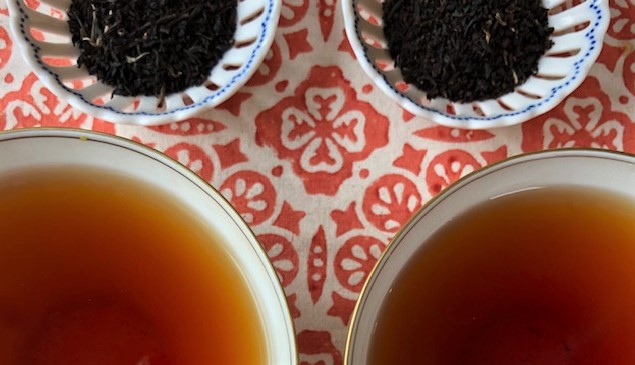 two cups of black tea with the dry tea leaves above them on an orange and white tablecloth