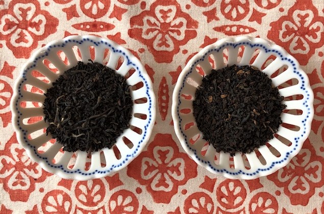 Two white porcelain bowls with blue rims holding tea leaves, set on an orange and white tablecloth.