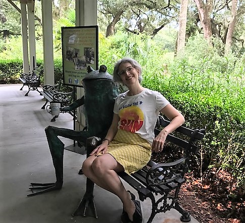 Metal statue of Waddy the Frog, the tea mascot from the Charleston Tea Garden, holding a mug of tea. Teainfusiast is seated next to Waddy on a bench