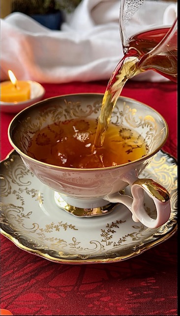 Black, white, and gold teacup and saucer on a bright red table cloth. Tea is pouring into the cup. Adding color can help you enjoy tea when you can't taste.