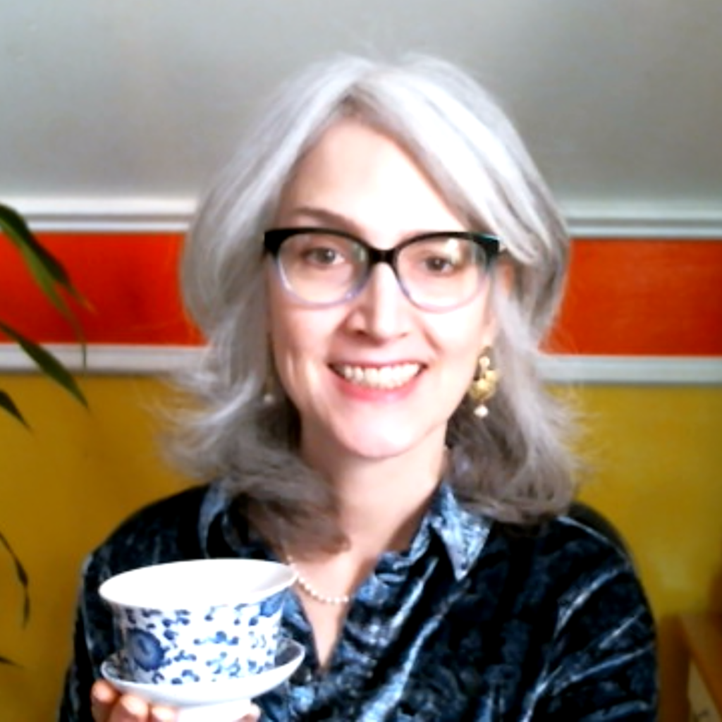Traci Levy, a woman with silvery salt & pepper hair wearing glasses, smiling, and holding a gaiwan without a lid.