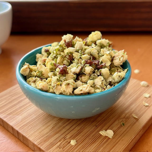 Plum Blossom herbal tea heaped in a blue dish sitting on a wooden coaster.