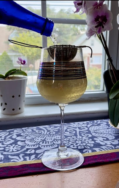 Rice oolong tea prepared sparking, pouring from a cobalt blue bottle through a tea strainer into a tall glass with blue and purple stripes