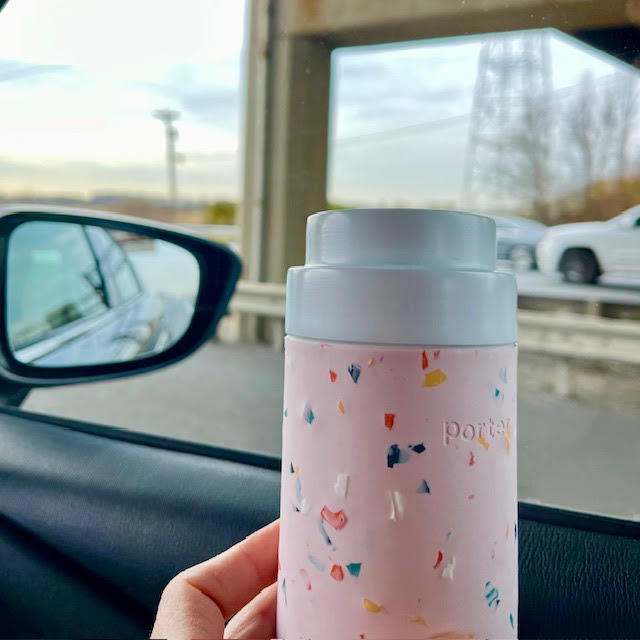 Pink thermos full of Black Saffron tea, held next to a car window with the New Jersey Turnpike in the background.