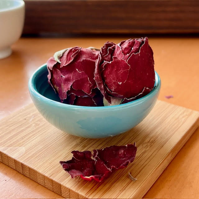 Crimson Rose herbal tea --two large red rosebuds in a blue dish sit on a wooden coaster.