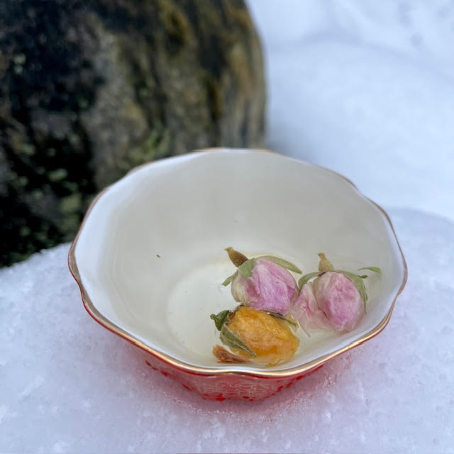 Red and gold Royal Grafton sugar bowl being used as a teacup. Inside, two pink rosebuds, a yellow rosebud, and a slice of dried quince make a lovely tisane.