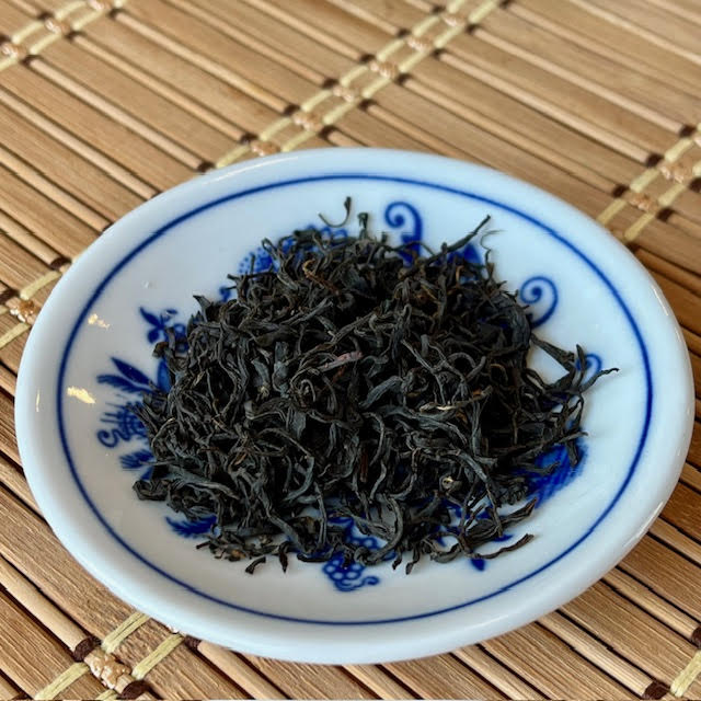 Black Dragonwell tea leaves in a white dish.