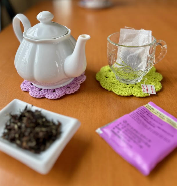 Loose leaf vs. tag bags--dish of loose leaf tea and a white teapot on one side and a glass teacup with a tea bag and tea bag wrapper on the other