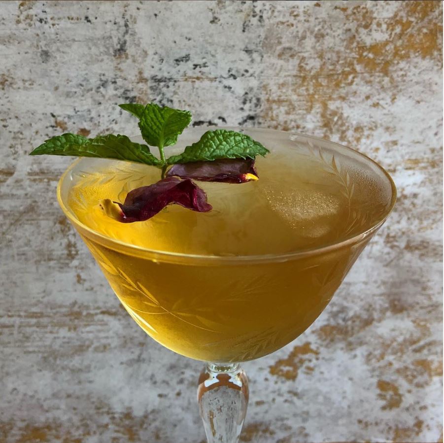 Demi-coupe glass of iced Feng Huang tea, garnished with red rose petals and a mint sprig