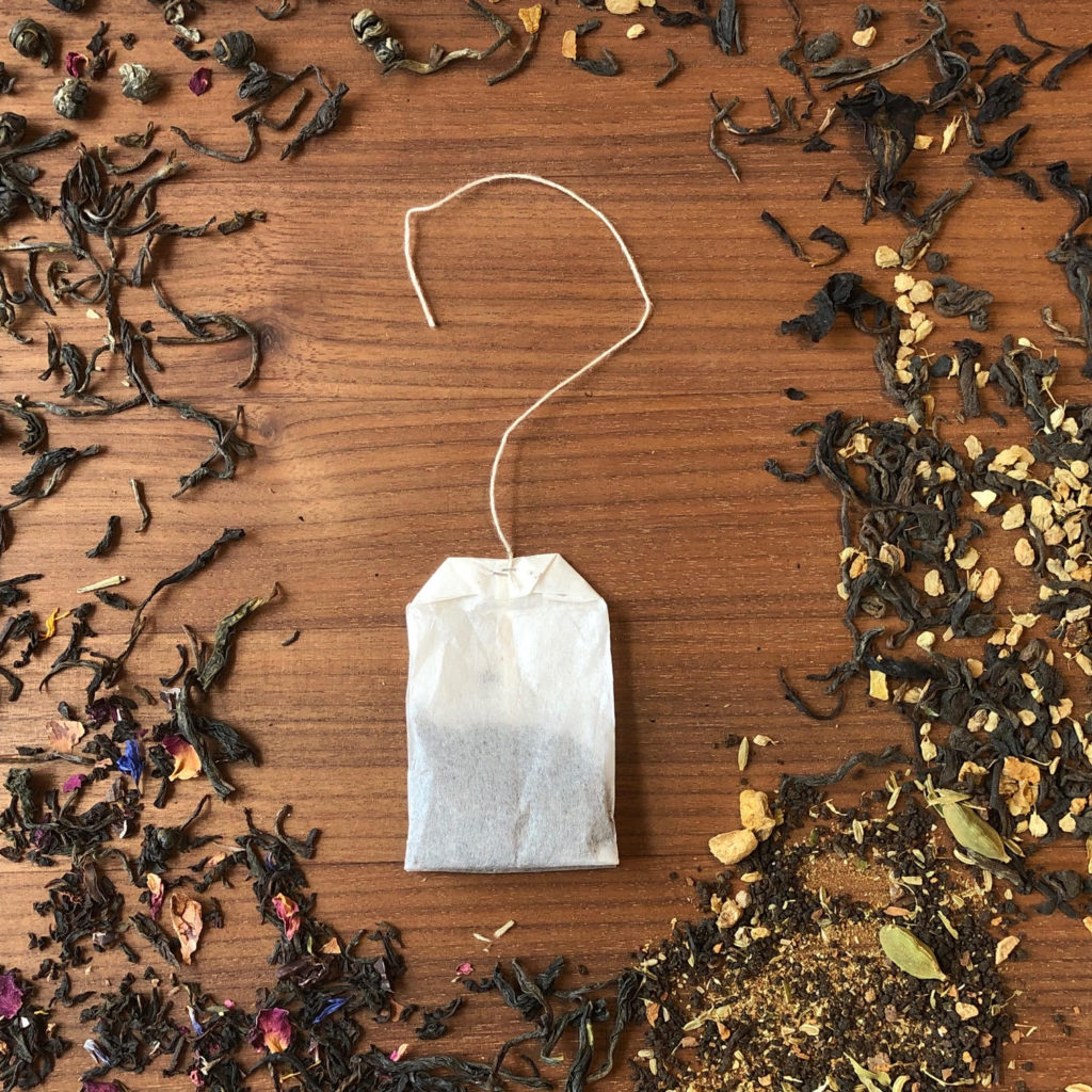 Picture of a tea bag, with the string curved into the shape of a question mark, surrounded by loose leaf tea