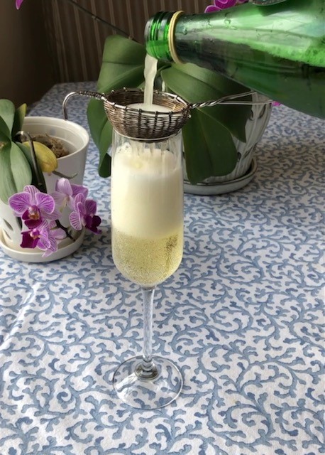 Pouring sparkling Balhyo Cha tea info a champagne flute through a tea strainer. An orchid is next to the glass.