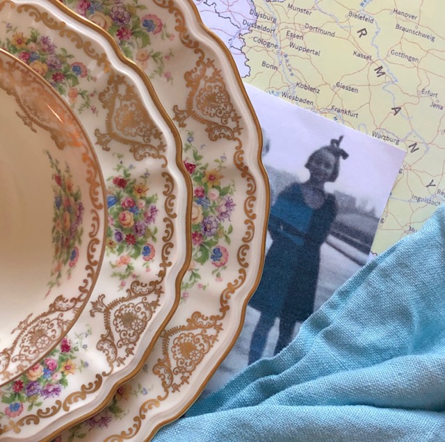 Teacup, saucer, and plate with floral and gold motif next to an old photo of a girl and a map