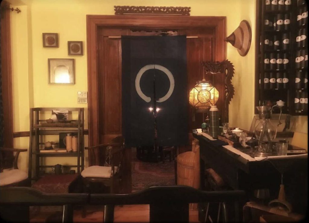 A view of an interior doorway inside Entheawith a dark hanging separating two rooms,, dark wooden furniture, and creamy yellow walls.