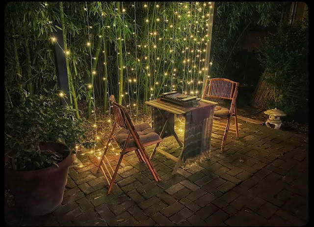 Photo of a tea tray on top of a small table surrounded by two chairs , bamboo plants, and fairy lights at night in the back courtyard at Enthea