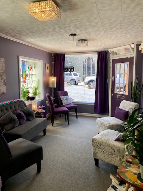 A room with purple and cream arm chairs, a gray loveseat with throw pillows, and purple curtains