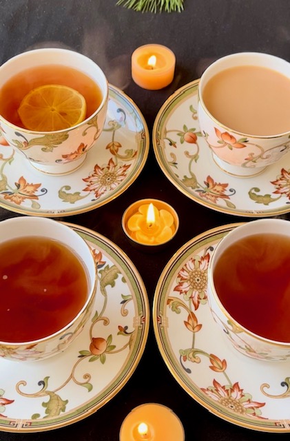 Four cups and saucers with tea arranged on a table with a candle in the center