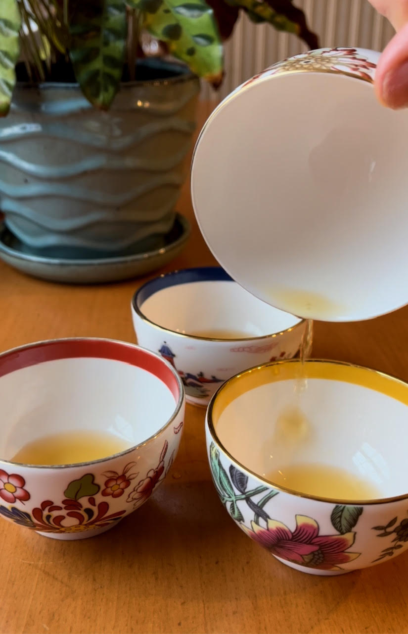 Trying to pour from an empty cup. Three teacups with almost no tea in them and a tiny bit of tea pouring from one cup into another.