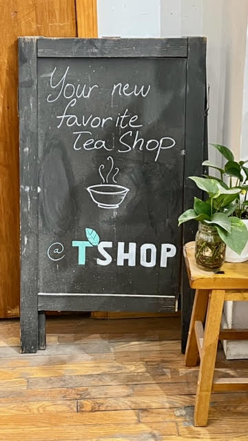 Chalkboard sign that says "Your new favorite tea shop: T-Shop." Ivy plants sit on a little table by the sign.