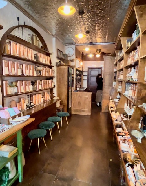 The interior of Paquita, a tearoom in Manhattan. Wooden shelves with copper canisters of teas and tisanes line the walls. A hammered tin ceiling adds ornate detail.