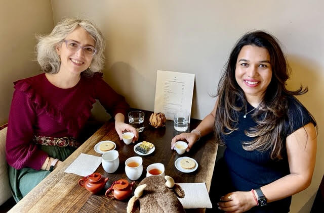 Two woman enjoying tea at Té in Manhattan, New York City. Small clay pots of tea, white fairness pitchers, teacups, and handmade tea snacks are on a wooden table.