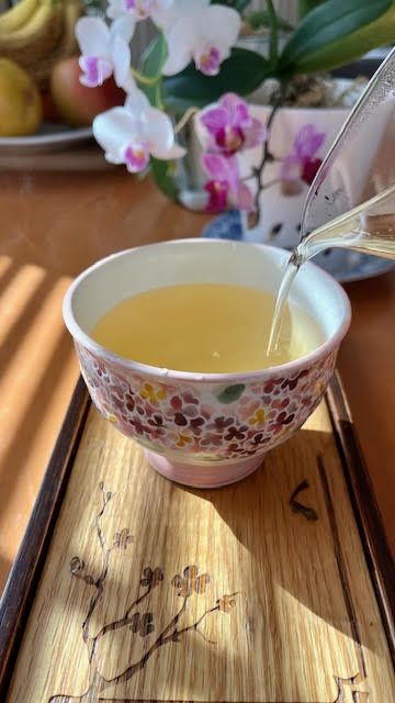 Tipsy Garden tea from Volition Tea--a beautiful golden yellow--pouring from a glass fairness pitcher into a floral teacup without handles.