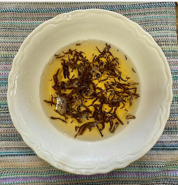 Bowl tea--cream colored bowl with scalloped edges containing loose leaf black tea and water.