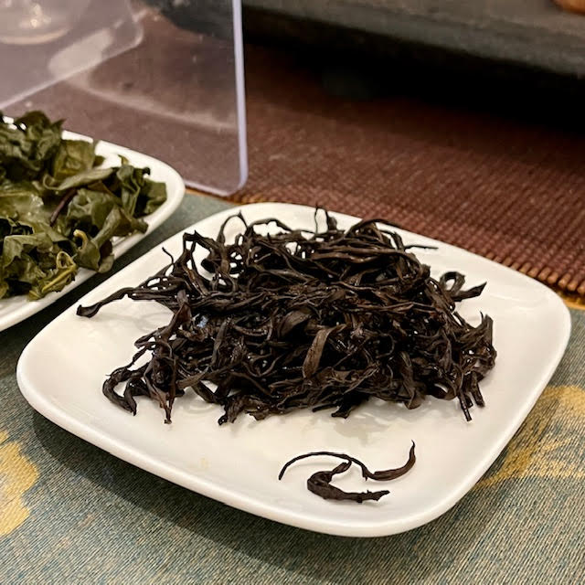 Dark brown Hadong Hwang Cha tea leaves after several infusions. One leaf pair looks like it's forming an old-fashioned letter "T" in calligraphy.