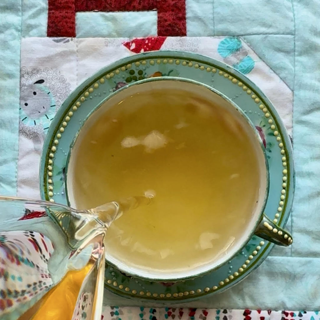 Pouring steeped Kashmiri Kahwa green tea with spices into a blue teacup with a yellow dot border