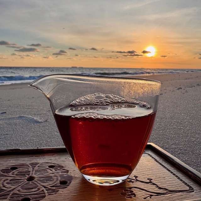 glass fairness pitcher (or gong dao bei) on a wooden tea tray on a beach
