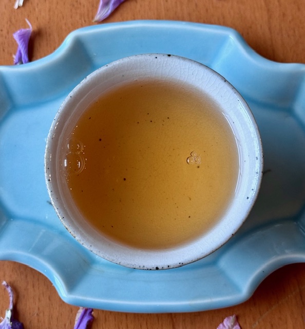 Amber-colored tea in a white speckled teacup sits on a sky blue tray