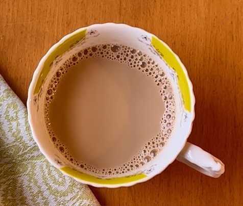 cup of tea with milk in a white mug with yellow details next to a white and green cloth napkin