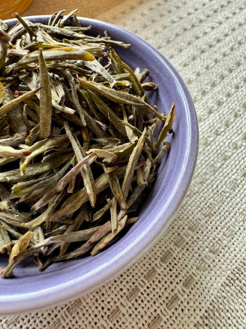 Close up of half a purple dish with yellow tea tea leaves--small, pointed buds and leaves that are green and yellow-green
