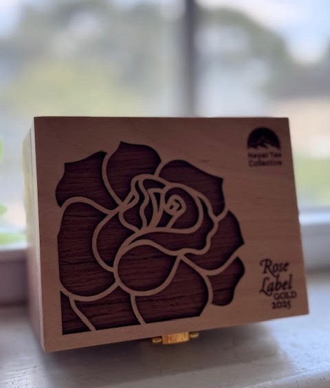 Wooden box with a rose carved on the top. In one corner it says "Nepal Tea Collective." In another it says "Rose Label Gold 2025."