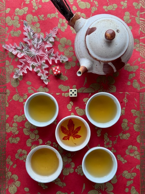 5 small cups of tea next to a white and brown kyusu teapot and a crystal snowflake on top of a red and gold background