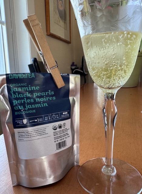 a delightful 2025 find--a bag of Jasmine Black Pearls tea next to a wine glass of the sparkling tea
