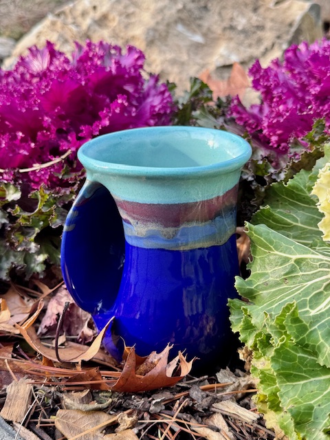 Side view of Handwarmer Mug from Neher Pottery next to some fuschia winter cabbage plants