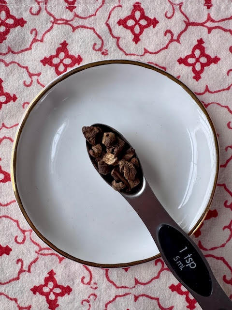 a silver 1 tsp measuring spoon full of burdock root tea on top of a white dish