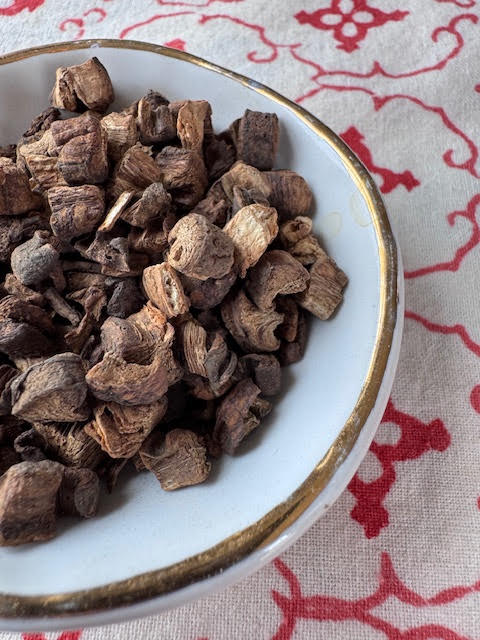 A white dish with a gold rim filled with burdock root, looking like small pieces of dried wood