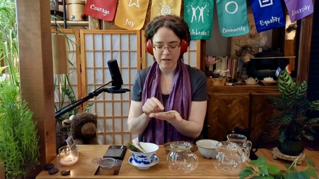 Sooz Hammond of Being Tea showing their love of tea by handling the tea loves on air in their studio. Sooz has dark short hair and is wearing red headphones