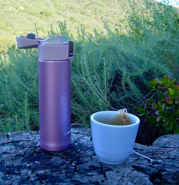 Zojirushi thermos or stainless mug--lavender--next to a white teacup with a teabag on a tree stump