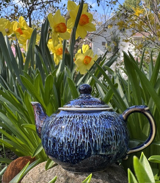 Blue glazed teapot from Umi Tea Set Starry Skies Jian Zhan Tea Set. The teapot sits on a rock and daffodils are in the background.