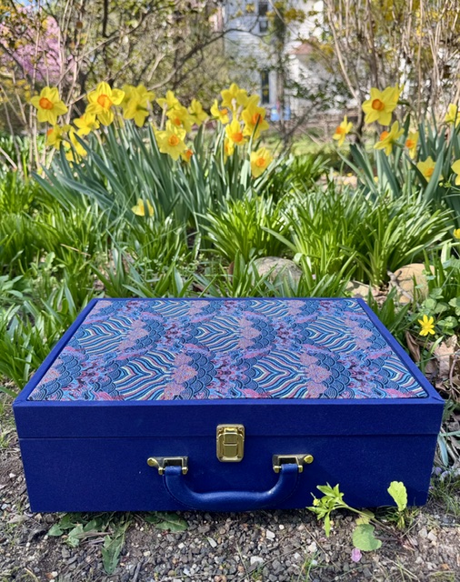 Blue carrying case with a fabric top and a blue handle in front of daffodils