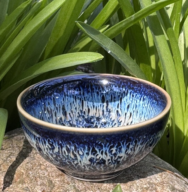 Small, handless teacup with blue glaze "Starry Sky Tea Set" from Umi Tea Sets on a rock next to the leaves of daffodils