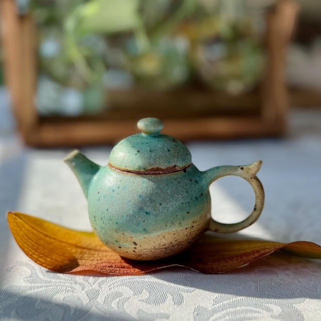 tiny glazed teapot (blue and brown) on a golden, dried orchid leaf