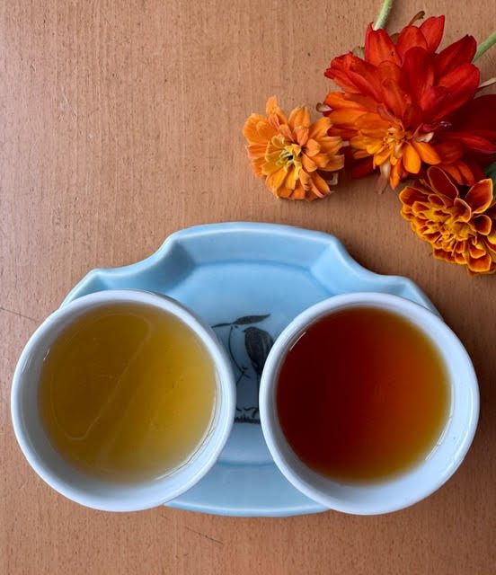 green and red rooibos in white cups side by side next to orange and red flowers