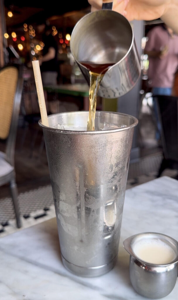 Pouring hot tea over tall silver cup full of ice at Witches Brew on Long Island