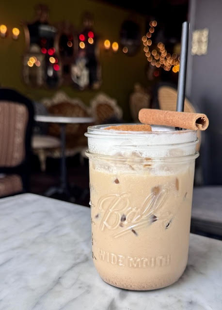 Glass jar with an iced chai. A cinnamon stick is on top and a metal straw pokes out of the iced tea.